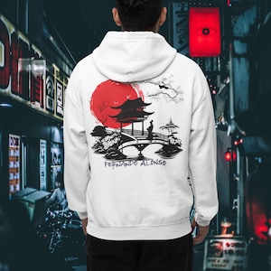 Może przedstawiać: Biała bluza z kapturem z japońskim wzorem na plecach. Grafika zawiera czerwone słońce, pagodę, most i postać. Nazwa "FERNANDO ALONSO" jest wydrukowana poniżej na niebiesko. Bluza ma kaptur i przednią kieszeń.