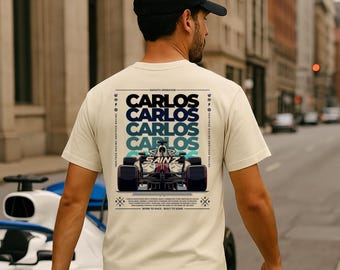 Peut inclure: Un t-shirt beige avec un imprimé graphique d'une voiture de course et le texte "Carlos" répété quatre fois. Le texte "Sainz" est également visible sur la voiture. Le texte "Smooth Operator" et "Born to Race - Built to Soar" est également imprimé sur le t-shirt.