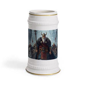 Pode incluir: Uma caneca de cerveja de cerâmica branca com um gráfico central de um guerreiro barbudo com capacete de chifres e capa com acabamento em pele, segurando um cajado. A caneca tem borda e base texturizadas com linhas douradas nas extremidades.