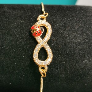 May include: A gold infinity symbol bracelet with clear rhinestones and a red ladybug charm.
