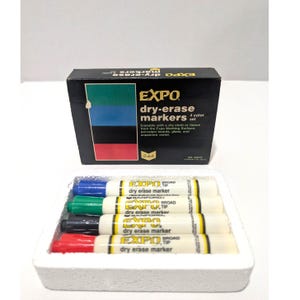 May include: A set of EXPO dry-erase markers in a black box and a white foam tray. The box displays the brand name and a color chart. The tray holds four markers: blue, green, black, and red. Each marker has a white barrel and black text.