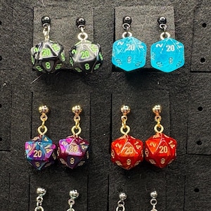May include: Four pairs of dangle earrings featuring miniature twenty-sided dice as charms. The dice come in black with green numbers, bright blue, iridescent purple and pink, and solid red with gold numbers, all attached to small metal posts.