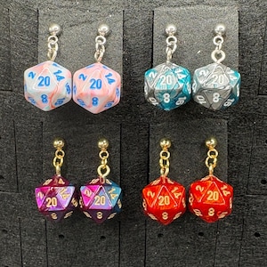 May include: Four pairs of dangle earrings featuring polyhedral dice. The dice are in various colors, including pink, blue, teal, gray, purple, and red. Each die has the number 20 visible, and the earrings have silver or gold-colored findings.