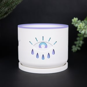 May include: White ceramic planter with a purple rim and a blue and purple eye design with raindrops.