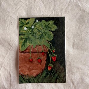 May include: A rectangular painting featuring a terracotta-colored pot containing a strawberry plant with green leaves, small white flowers, and several bright red strawberries hanging over the rim against a dark, textured background.