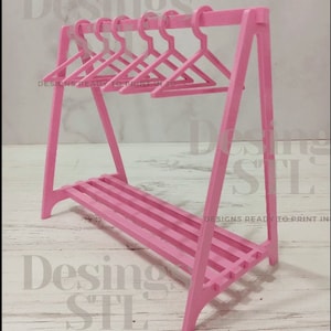 May include: Pink plastic doll-sized clothing rack with a shelf and six pink hangers.