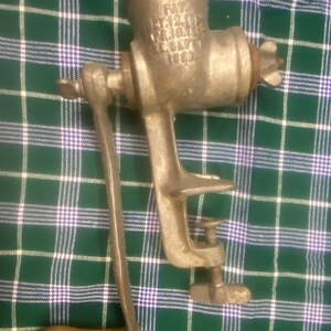 May include: A vintage, cast-iron meat grinder with a wooden handle and a clamp for securing it to a surface. The grinder has a crank handle and a star-shaped tightening knob. The text "PAT. DEC. 24, 1918" is visible on the grinder's body.