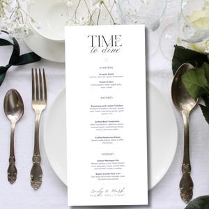 Puede incluir: Una tarjeta de menú blanca con el texto "Time to Dine" en letras negras. El menú enumera aperitivos, platos principales y postres. La parte inferior de la tarjeta tiene los nombres "Emily & Mark" y la fecha "07.02.2023".