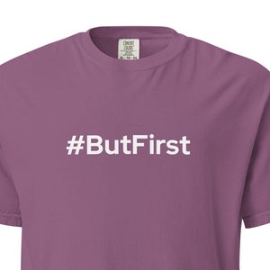 May include: A mauve-colored t-shirt with the text "#ButFirst" printed in white. The shirt has short sleeves and a crew neck. The text is centered on the front of the shirt.