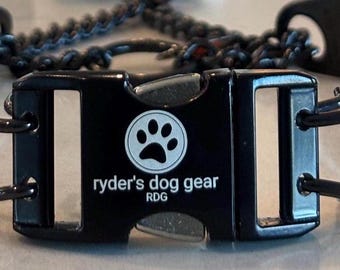 Op de afbeelding: Close-up van een zwarte hondenriemgesp met de tekst "ryder's dog gear" en een pootafdruklogo. De gesp maakt deel uit van een hondenriem met een zwart en blauw gevlochten ontwerp.