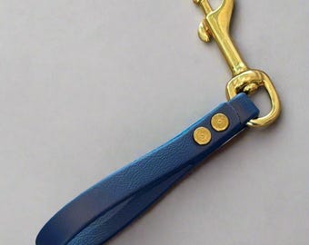 Könnte beinhalten: Ein blauer Leder-Hundeleinen-Griff mit einem goldfarbenen Metallverschluss und Nieten. Der Griff hat eine tiefblaue Farbe und scheint aus hochwertigem Leder gefertigt zu sein. Der Verschluss ist goldfarben.