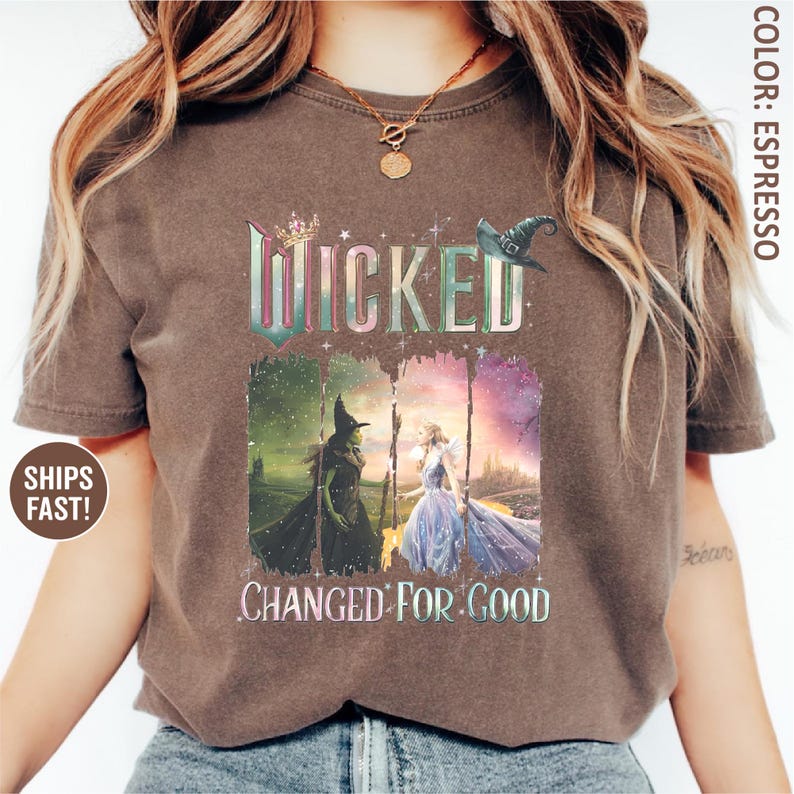 May include: Espresso-colored t-shirt featuring the word "Wicked" in a colorful, distressed font. Below, the phrase "Changed for Good" is displayed. The shirt showcases a graphic of two characters from the musical, one in green and the other in a blue gown.