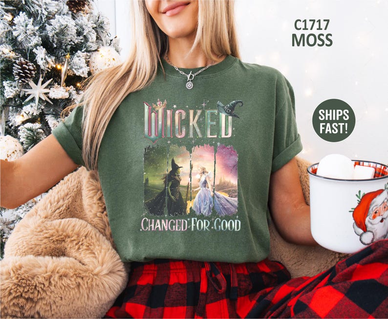May include: Moss green t-shirt featuring the word "Wicked" in a colorful, glittery font, with an image of two witches. The phrase "Changed For Good" is printed below the image. The shirt is a comfortable, casual style.