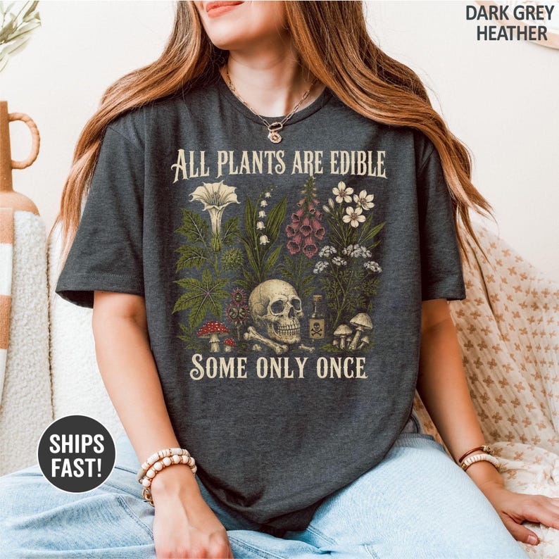 Pu&ograve; includere: T-shirt grigio scuro melange con la scritta "ALL PLANTS ARE EDIBLE SOME ONLY ONCE". La grafica presenta varie piante, un teschio e funghi. La maglietta &egrave; un capo comodo e casual.