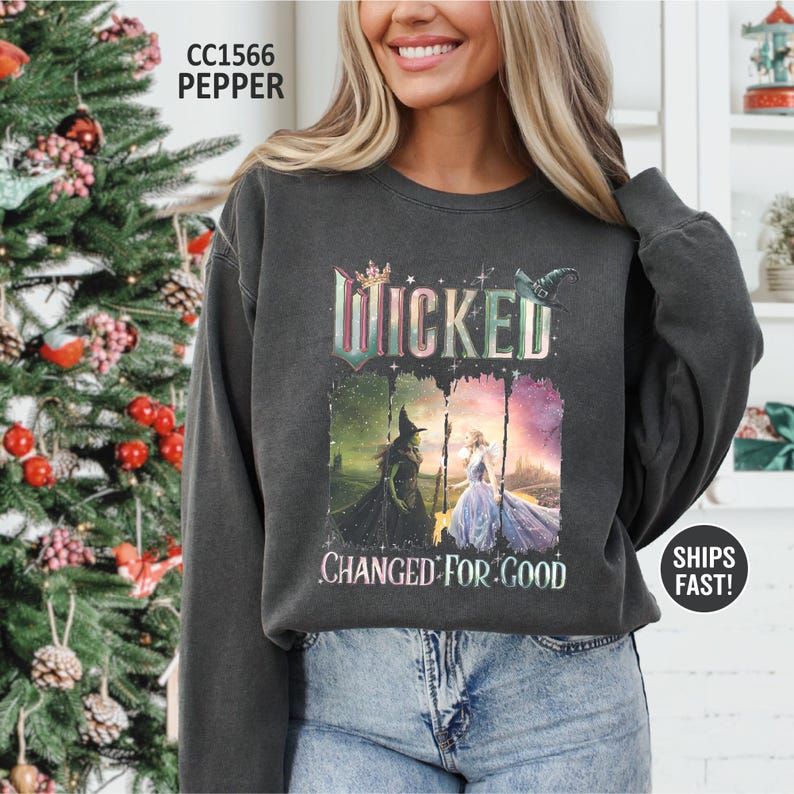May include: Dark gray sweatshirt featuring the word "Wicked" above a graphic of two characters from the musical. The text "Changed For Good" is below the graphic. The sweatshirt is a crew neck style.