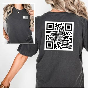 May include: A dark gray t-shirt with a black and white QR code printed on the back. The shirt has a crew neck and short sleeves.