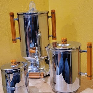 May include: A set of three vintage chrome coffee and tea pots with wooden handles. The pots have a polished chrome finish and are in excellent condition.
