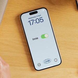 Op de afbeelding: Een smartphone-scherm dat de tijd 17:05, de datum woensdag 9 april en het woord "Innie" met een groene schuifknop weergeeft. Het scherm toont ook een logo voor "LUMON" en een camera-icoon.