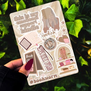 Op de afbeelding: Een set van 10 boekenstickers met illustraties van boeken, koffiebekers en een kat. De stickers zijn op een witte achtergrond met een marmerpatroon. De tekst op de stickers is "This is my emotional support kindle", "Bookish", "Reading fuel", "Just one more chapter", "Book Club" en "#bookworm".