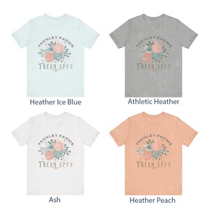 May include: Four different color t-shirts with a graphic design of yarn balls and leaves with the text "Yarnley Farms Fresh Spun". The colors are Heather Ice Blue, Athletic Heather, Ash, and Heather Peach.