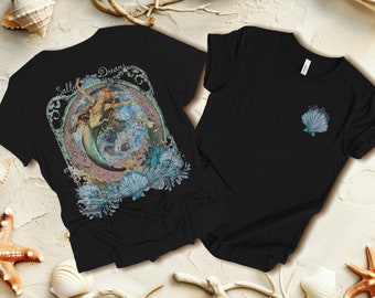 Puede incluir: Camiseta negra con un gráfico de sirena y el texto "Salty Dream" en la espalda. La parte delantera de la camiseta tiene un pequeño gráfico de concha.