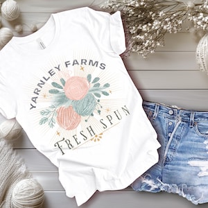 May include: White t-shirt with a graphic design of yarn balls and the text "Yarnley Farms Fresh Spun".