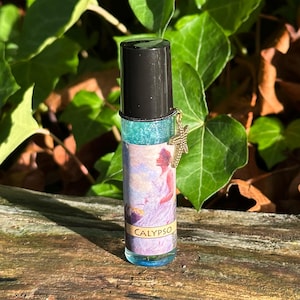 May include: A glass roller bottle with a black cap and a gold-colored cross charm. The bottle contains a blue liquid with glitter and a label that reads "CALYPSO". The label features an illustration of a woman in a flowing gown.