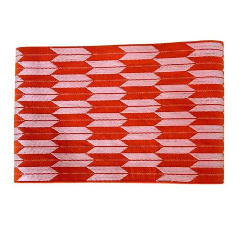 May include: A rectangular fabric piece featuring a repeating arrow pattern in vibrant orange and soft pink. The design consists of horizontal rows of stylized, pointed arrow shapes that alternate in color, creating a consistent geometric texture.