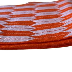 May include: A vibrant orange fabric band featuring a repeating white arrow-like pattern. The material has a textured, woven appearance with a distinct horizontal orientation, showcasing a consistent geometric design across the entire surface.
