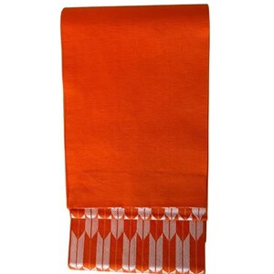 May include: A rectangular textile piece in a vibrant orange hue. The upper section features a solid, smooth orange surface, while the lower portion displays a repeating pattern of vertical white arrow-like shapes set against the same orange background.