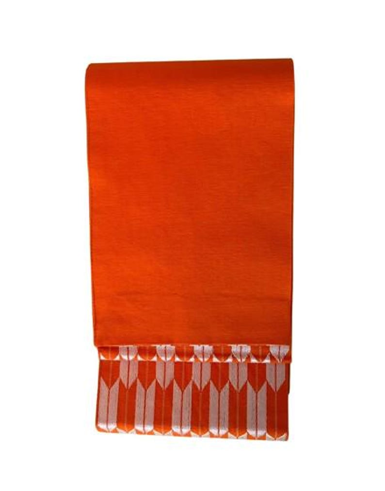 May include: A rectangular textile piece in a vibrant orange hue. The upper section features a solid, smooth orange surface, while the lower portion displays a repeating pattern of vertical white arrow-like shapes set against the same orange background.