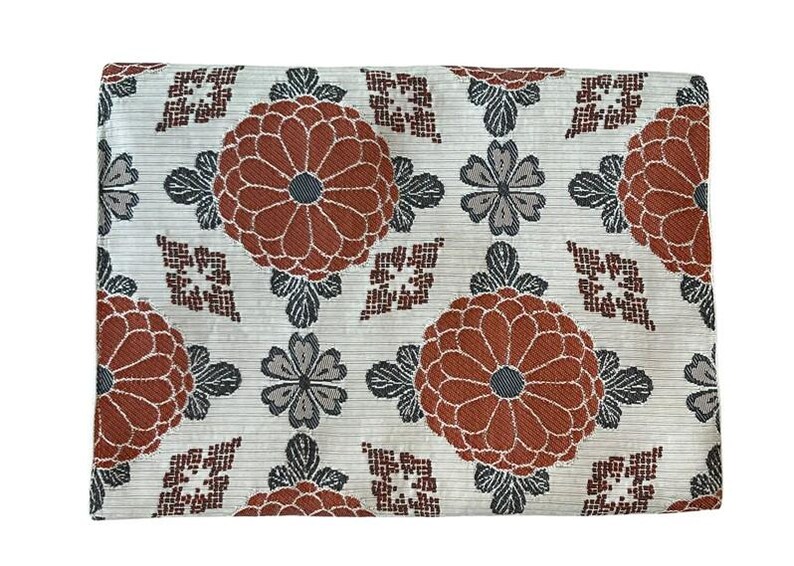May include: A rectangular fabric piece featuring a repeating pattern of large rust-orange chrysanthemum-like flowers, smaller grey four-petaled blossoms, and dark brown geometric diamond shapes set against a light grey textured background.