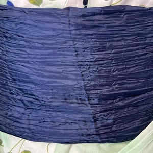 Op de afbeelding: Een brede, donker marineblauwe sjerp met een zwaar gekreukelde, horizontale textuur. De stof heeft een subtiele glans en is gewikkeld rond een lichtgekleurd kledingstuk dat een vaag, lichtgroen en blauw bloemenpatroon op het oppervlak toont.