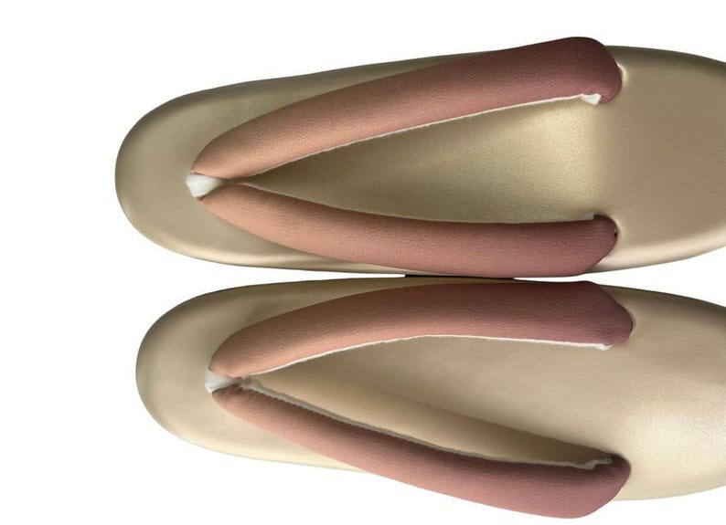 May include: A pair of traditional Japanese geta sandals. The sandals have a light beige base with two straps in a gradient of pink and brown. The thong straps are padded for comfort. The sandals are designed for outdoor wear.
