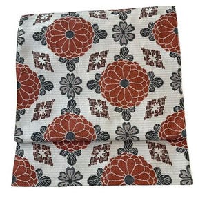 May include: A rectangular textile featuring a repeating pattern of large, rust-orange chrysanthemum-like flowers, smaller grey floral motifs, and geometric diamond shapes set against a cream-coloured background with fine horizontal line textures.