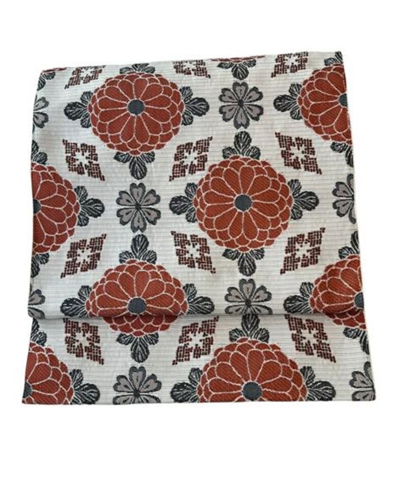 May include: A rectangular textile featuring a repeating pattern of large, rust-orange chrysanthemum-like flowers, smaller grey floral motifs, and geometric diamond shapes set against a cream-coloured background with fine horizontal line textures.