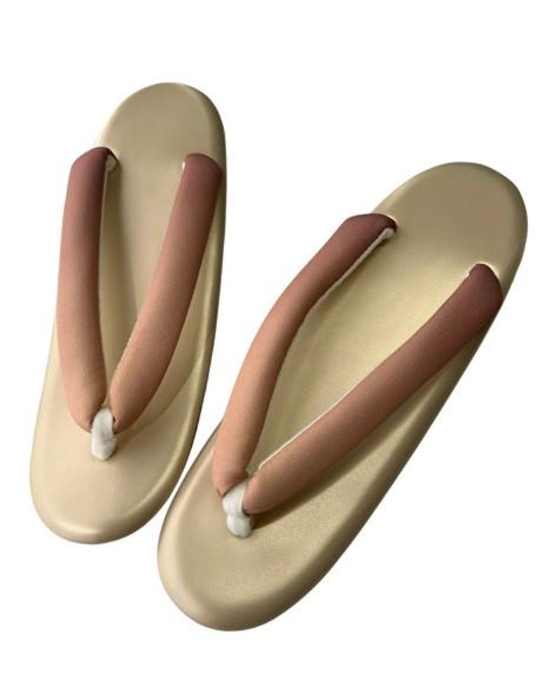 May include: A pair of traditional Japanese geta sandals. The sandals have a light beige base with brown and beige straps. The straps are padded for comfort. The geta sandals are designed to be worn with traditional Japanese clothing.