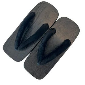 May include: A pair of geta sandals featuring dark brown wooden platforms with a visible wood grain texture. Each sandal has a thick, black fabric thong strap attached to the center and sides of the rectangular base, designed for foot placement.
