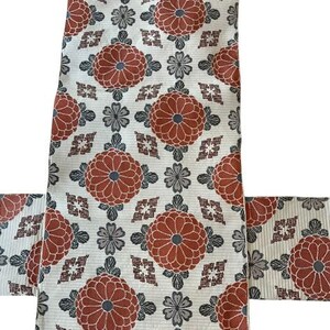 May include: A textile fabric featuring a repeating pattern of large, rust-orange circular floral motifs interspersed with smaller grey flower shapes and geometric diamond-like accents on a cream-coloured background with fine horizontal lines.