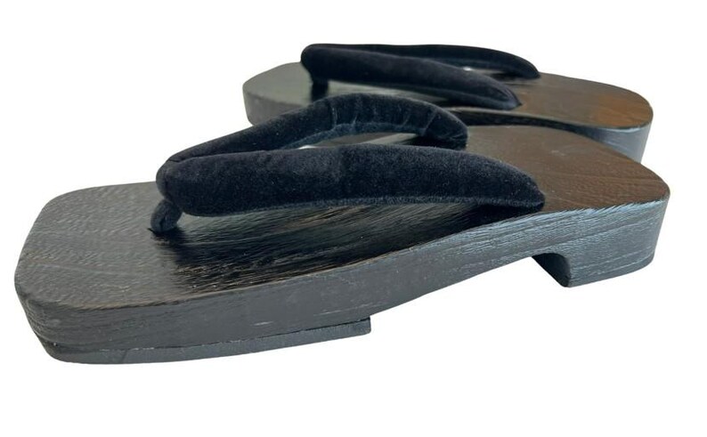 May include: A pair of geta sandals featuring dark brown wooden platforms with a visible wood grain texture and thick, black velvet thong straps. The sandals have a rectangular base with a raised heel support and a flat front section.