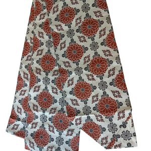 May include: A long, rectangular textile strip featuring a repeating pattern of large, rust-orange chrysanthemum-style floral motifs interspersed with smaller, dark grey floral shapes and geometric diamond-like accents on a cream-coloured background.