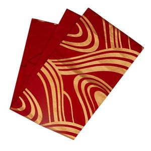 May include: Red fabric with a gold, wave-like pattern. The fabric is folded, revealing a solid red underside. The gold design features curved lines and shapes, creating a flowing, abstract design. The fabric appears to be a decorative textile.