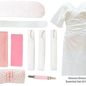 May include: A white kimono dressing essential set of 10 items including a white robe, a pink patterned obi pillow, a pink mesh sash, a pink rectangular pad, three white ties, a white belt, a pink clip, and a white headpiece.
