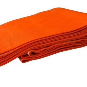 May include: A folded rectangular textile piece featuring a solid vibrant orange color on one side and a pattern of alternating orange and white horizontal stripes on the reverse side, showing a textured knit construction throughout the fabric.