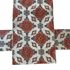 May include: A textile fabric featuring a repeating pattern of large, circular, rust-coloured floral motifs interspersed with smaller, grey, four-petaled blossoms and geometric diamond shapes on a textured, off-white background.