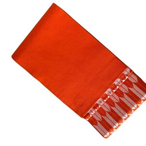 May include: A vibrant orange fabric textile featuring a decorative border along one edge. The border displays a repeating pattern of white, arrow-like shapes arranged in a horizontal row, creating a distinct contrast against the solid orange background.