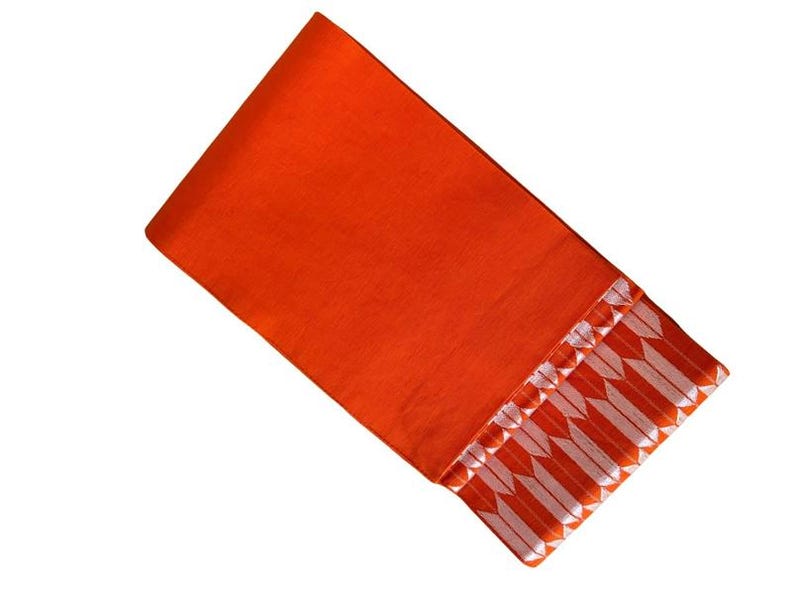 May include: A vibrant orange fabric textile featuring a decorative border along one edge. The border displays a repeating pattern of white, arrow-like shapes arranged in a horizontal row, creating a distinct contrast against the solid orange background.