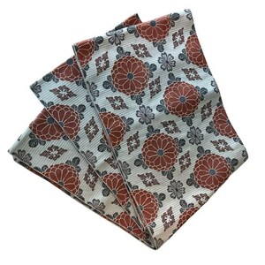 May include: A folded textile featuring a repeating pattern of rust-coloured chrysanthemum flowers, small grey floral accents, and geometric diamond shapes on a light blue background with a fine, vertical ribbed texture throughout the fabric surface.