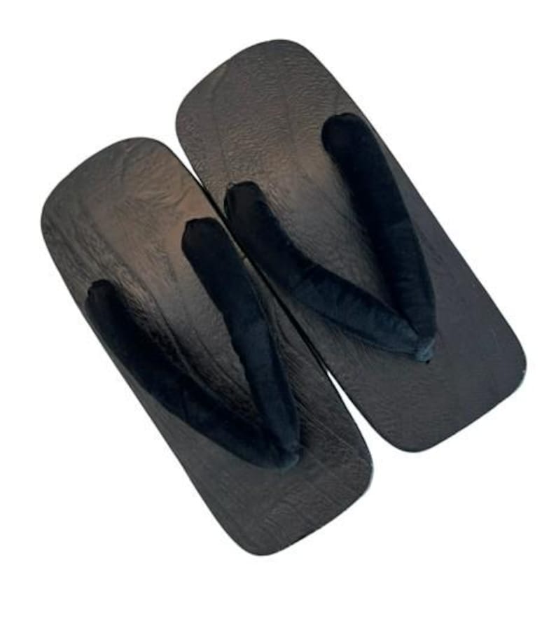 May include: A pair of traditional Japanese geta sandals featuring rectangular dark brown wooden bases with a visible wood grain texture and thick, soft black fabric thong straps positioned in a V-shape across the top of each sandal.