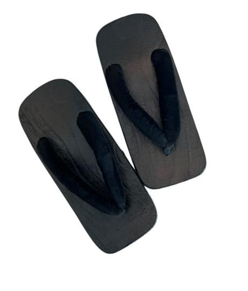 May include: A pair of traditional Japanese geta sandals featuring dark brown wooden platforms with a visible wood grain texture and soft black fabric thong straps. The rectangular base design provides a flat surface for the foot with a rounded toe.